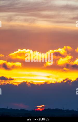 Sonnenaufgang über dem Südosten Kents mit der Sonne, die rot erscheint, durch schwere dunkle Wolken am Horizont mit gelbem Himmel mit vielen Wolken darüber. Stockfoto