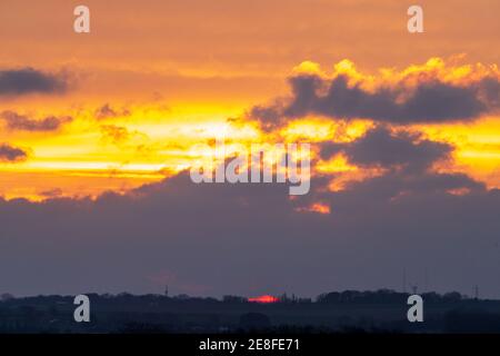 Sonnenaufgang über dem Südosten Kents mit der Sonne, die rot erscheint, durch schwere dunkle Wolken am Horizont mit gelbem Himmel mit vielen Wolken darüber. Stockfoto