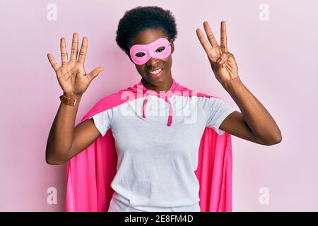 Junge afroamerikanische Mädchen trägt Superhelden Maske und Cape Kostüm Zeigen und zeigen mit den Fingern Nummer acht beim Lächeln Selbstbewusst und happ Stockfoto