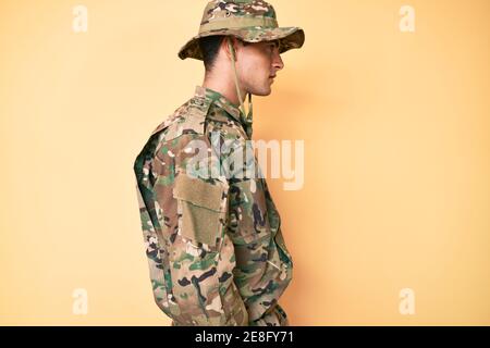 Junge gutaussehende Mann trägt Tarnung Armee Uniform suchen zur Seite, entspannen Profil Pose mit natürlichen Gesicht mit selbstbewussten Lächeln. Stockfoto