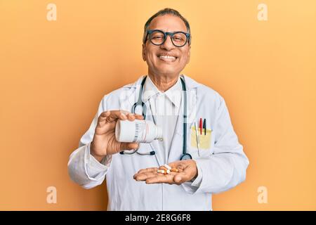 Mittelalter indischer Mann trägt Arzt Uniform hält verschreibungspflichtige Pillen lächeln mit einem glücklichen und kühlen Lächeln auf Gesicht. Zeige Zähne. Stockfoto
