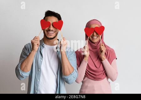 Romantisches muslimisches Paar, das die Augen mit roten Papierherzen bedeckt Stöcke Stockfoto