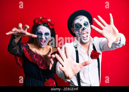Schönes Paar trägt Tag der Toten Kostüm gestikuliert als Zombie über isolierten roten Hintergrund. Stockfoto