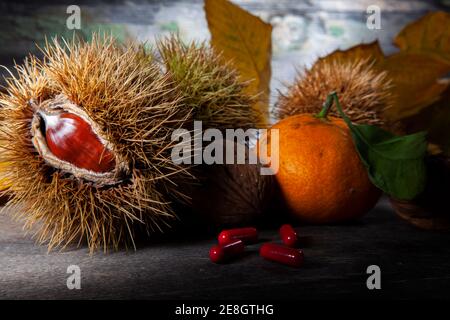 Herbst Stillleben von Kastanie, Mandarine und Pillen. Makrofoto von auf Holztisch mit verfallener Hintergrund. Aufgenommen mit Spotlight in Studio Stockfoto