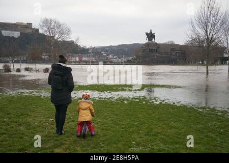 Koblenz, Deutschland. Januar 2021. Eine Familie steht auf einer teilweise überfluteten Wiese am Moselufer gegenüber dem Deutschen Eck mit der Reiterstatue von Kaiser Wilhelm. Schmelzender Schnee und heftige Regenfälle haben dazu geführt, dass der Wasserstand ansteigt. Quelle: Thomas Frey/dpa/Alamy Live News Stockfoto