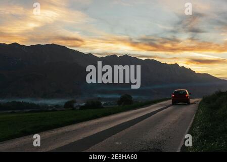 Autofahren entlang der Asphaltstraße auf dem Hintergrund der Bergkette Unter Sonnenuntergang am Himmel am Abend Stockfoto