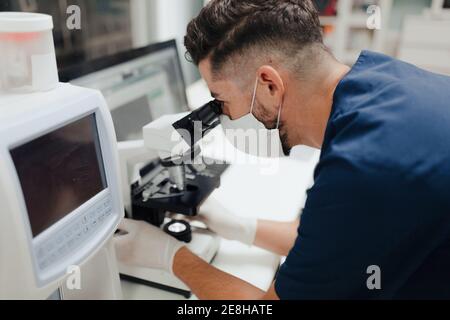 Seitenansicht der Ernte anonymen männlichen Sanitäter in Uniform und Maske mit Mikroskop während der Arbeit im Labor Stockfoto