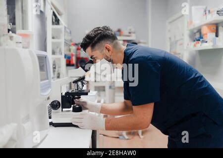 Seitenansicht der Ernte anonymen männlichen Sanitäter in Uniform und Maske mit Mikroskop während der Arbeit im Labor Stockfoto