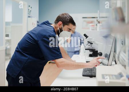 Seitenansicht der Ernte anonymen männlichen Sanitäter in Uniform und Maske mit Mikroskop während der Arbeit im Labor Stockfoto