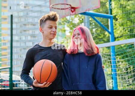 Portrait von Kerl und Teenager-Mädchen umarmt auf Basketballplatz Mit Ball in den Händen Stockfoto