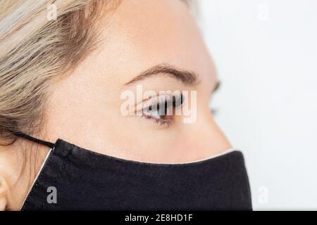 Crop ruhig junge Frau in schwarz Gesichtsmaske mit permanent Wimpern Verlängerung auf dem rechten Auge wegschauen Stockfoto