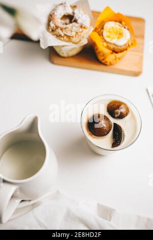 Draufsicht Komposition von süßen Schokoladenbomben, die im Glas schmelzen Von frischer heißer Milch auf dem Tisch in der Nähe von leckeren Cupcakes platziert Und Milchkännchen Stockfoto