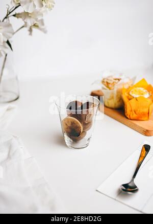 Zusammensetzung der süßen Schokolade Bomben schmelzen in Glas von frischen Heiße Milch auf dem Tisch in der Nähe von leckeren Cupcakes und Milch Kanne Stockfoto