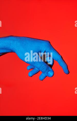 Der blaue Finger des Mannes zeigt nach unten auf rotem Hintergrund. Isoliertes vertikales Foto Stockfoto