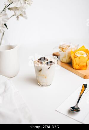 Zusammensetzung der süßen Schokolade Bomben schmelzen in Glas von frischen Heiße Milch auf dem Tisch in der Nähe von leckeren Cupcakes und Milch Kanne Stockfoto