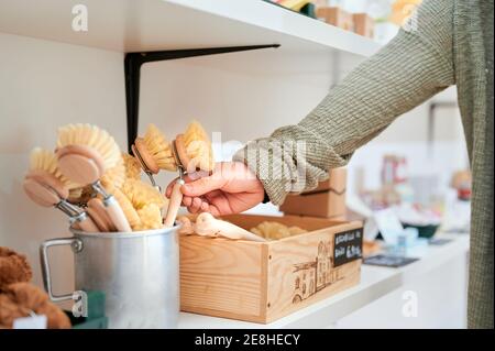 Crop anonyme weibliche Client unter Holzbürste aus Behälter während Einkaufen in Zero Waste Shop Stockfoto