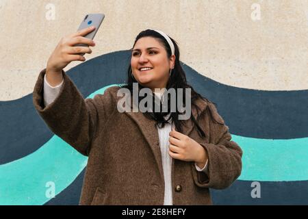 Weibliche Tourist in Hut sitzt auf Stein und Beobachtung landschaftlich Blick auf die Berge am bewölkten Tag entfernt Stockfoto