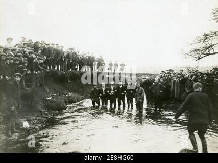 Ashbourne Shrovetide Football Anfang des 20. Jahrhunderts, wahrscheinlich in den 1910er oder 1920er Jahren genommen, einige Spieler aus den up'ards im Wasser des Henmore Brook und andere auf der Bank bei Sturston Mill mit einem Tor erzielt Stockfoto