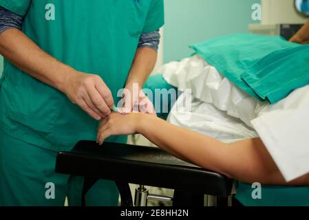Schneiden Sie nicht erkennbare medizinische Assistenten, die intravenösen Katheter in der Hand auf Anonymer Patient, der im Operationssaal auf der Couch liegt Stockfoto