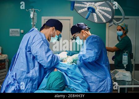 Nicht erkennbarer Patient, der während der Operation auf dem Operationstisch liegt Konzentrierte männliche Ärzte in medizinischen Kleidern und Masken Stockfoto