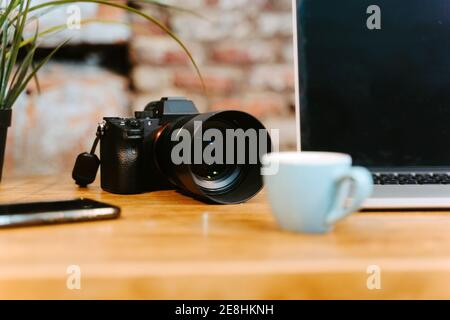 Arbeitsplatz des Freiberuflers mit modernen Netbook und professionelle Fotokamera Platziert auf Holztisch mit Tassen Espresso und Notizblock Im Café Stockfoto