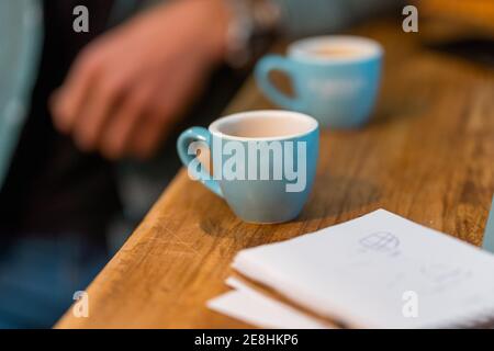 Kleine Tassen für Espresso auf Holztheke mit Notebook platziert Auf dem Hintergrund der Ernte nicht erkennbar Barista arbeitet im Café Stockfoto