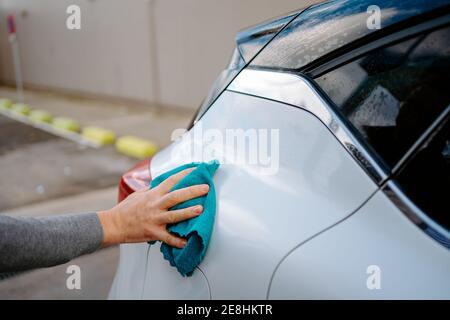 Cropped unkenntlich jungen männlichen Wischfahrzeug mit Lappen im Stehen In der Waschstation gegen bewölkten Himmel Stockfoto