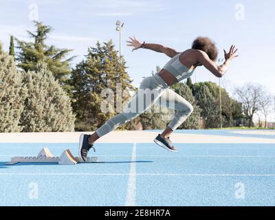 Seitenansicht der energiegeladenen afroamerikanischen Athletin, die ausläuft Der Startblöcke während des Trainings im Stadion Stockfoto