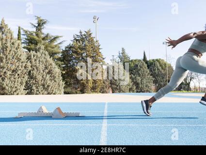 Seitenansicht der energiegeladenen afroamerikanischen Athletin, die ausläuft Der Startblöcke während des Trainings im Stadion Stockfoto