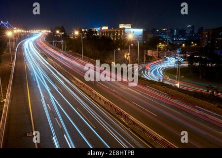 Langzeitbelichtung belebte Asphaltstraße mit fahrenden Fahrzeugen in zeitgenössischem Urbane Metropole bei Nacht Stockfoto