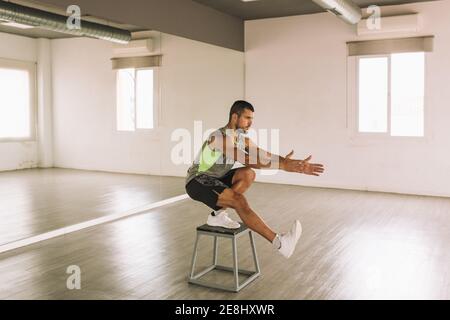 Seitenansicht von serious Young fit athletischen Mann in activewear Eine Bein Squat Übung auf Schritt Plattform während des Trainings Im Studio Stockfoto