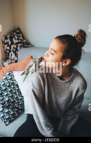 Junge weibliche Besitzer in legere Kleidung Vorbereitung zu küssen liebenswert Kakadus sitzt auf der Schulter im Wohnzimmer Stockfoto