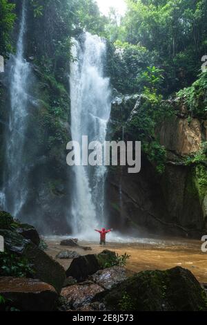 Rückansicht des nicht erkennbaren Reisenden in warmer Kleidung, die innen steht Teichwasser mit ausgestreckten Armen in der Nähe des malerischen Haew Narok Wasserfalls Streaming-thr Stockfoto