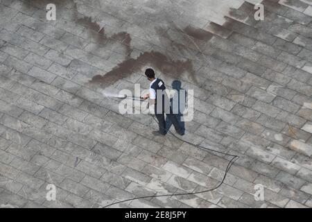 Mann Reinigung Boden mit Hochdruck Wasserstrahl Spray und Schmutzwasser entfernen Stockfoto
