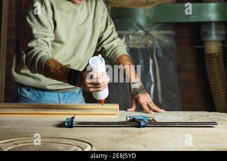 Unkenntlich Ernte reifen männlichen Zimmermann Anwendung Kleber auf Stück Holz beim Arbeiten am Tisch in der Schreinerei Stockfoto