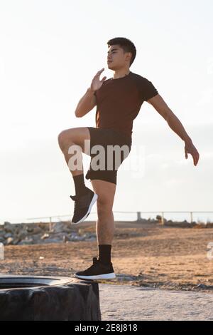 Ganzkörper-Seitenansicht des bestimmten jungen asiatischen männlichen in Sportbekleidung Durchführung Schritt Knie erhöhen Übung auf Reifen im Freien Fitnesstraining Stockfoto