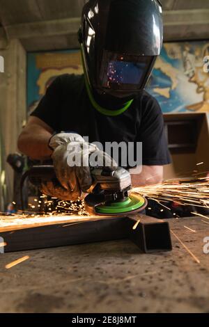 Unkenntlich männlichen Schweißer in Schutzhardhat mit elektrischen Mühle und Schneiden von Metall Detail in grungy Werkstatt Stockfoto