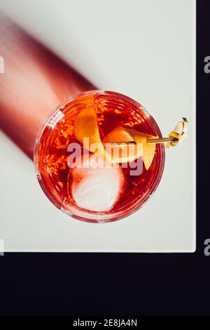 Glas bitteren alkoholischen Negroni Cocktail serviert mit Eis und Orangenschale auf weißer Oberfläche Stockfoto