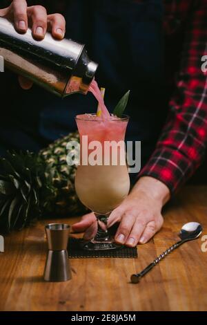 Crop anonyme Barkeeper in karierten Hemd Gießen alkoholische Pina Colada Vom Shaker ins Glas an der Theke Stockfoto