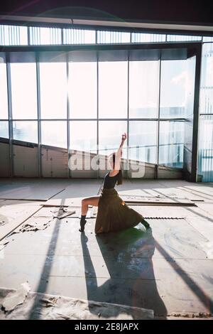 Seitenansicht einer weiblichen Theaterkünstlerin, die mit erhobenem Arm tanzt Blick auf die Kamera auf dem Boden mit Schatten gegen Glaswand Stockfoto