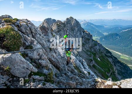 Bergsteiger steigt auf einem gesicherten Klettersteig, Mittenwalder Höhenweg, Blick ins Isartal bei Mittenwald, Karwendelgebirge, Mittenwald Stockfoto