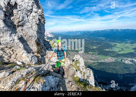 Bergsteiger steigt auf einem gesicherten Klettersteig, Mittenwalder Höhenweg, Blick auf Mittenwald, Karwendelgebirge, Mittenwald, Bayern, Deutschland Stockfoto