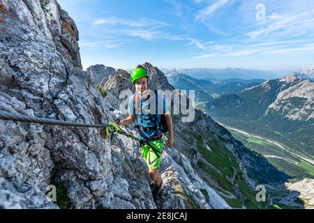 Bergsteiger steigt auf einem gesicherten Klettersteig, Mittenwalder Höhenweg, Blick ins Isartal bei Mittenwald, Karwendelgebirge, Mittenwald Stockfoto