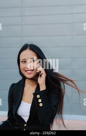 Eine frohe ethnische Geschäftsfrau, die auf der Straße steht und mit dem Handy spricht, während sie wegschaut Stockfoto