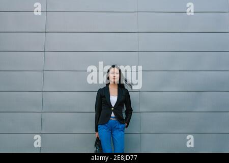 Selbstbewusste asiatische weibliche Unternehmerin auf der Straße in der Nähe stehen Städtisches Gebäude und Blick auf die Kamera Stockfoto