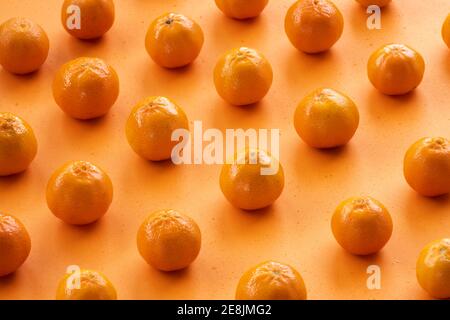 (Selektiver Fokus) flache Lage, Nahaufnahme einiger Mandarinen, die symmetrisch auf einem orangefarbenen Hintergrund angeordnet sind. Frisches Obst, Konzept der gesunden Ernährung. Stockfoto