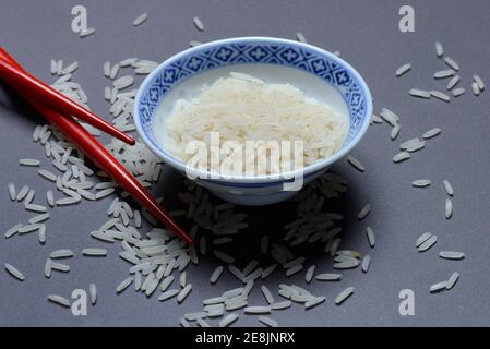 Reiskörner in Schale und Essstäbchen, Basmati-Reis, Oryza sativa, ungekocht Stockfoto