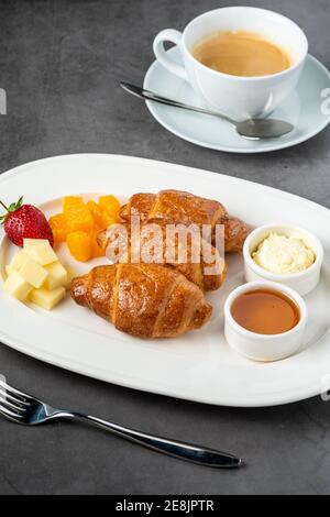 Französisches Croissant. Frisch gebackene Croissants mit Honig und Butter auf dunklem Steingrund. Stockfoto