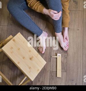 Eine Frau fiel von einer hölzernen Trittleiter und hält sich an ihrem schmerzenden Bein. Leiter aus Holz brach unter einem Mann während der Arbeit zu Hause Stockfoto