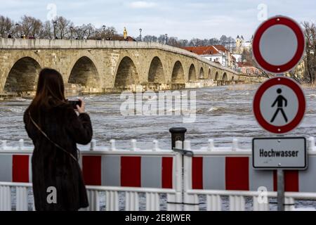 Regensburg, Deutschland. Januar 2021. Eine Frau fotografiert die überflutete Donau hinter einer Schranke vor der Steinernbrücke. Quelle: Armin Weigel/dpa/Alamy Live News Stockfoto